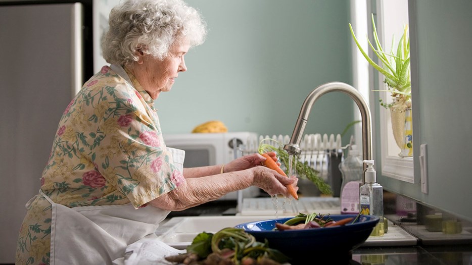 Äldre kvinna sköljer grönsaker.