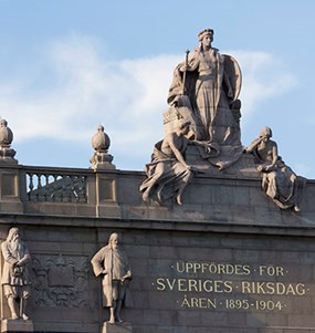 Stenskulpturer och svenska flaggan på riksdagshuset övre del.