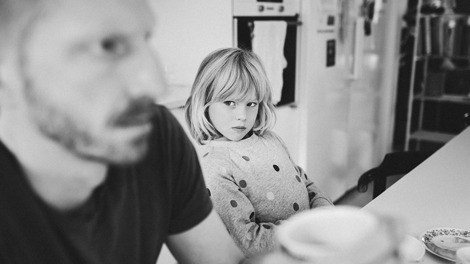 Litet barn tittar allvarligt på sin arga pappa vid ett köksbord.